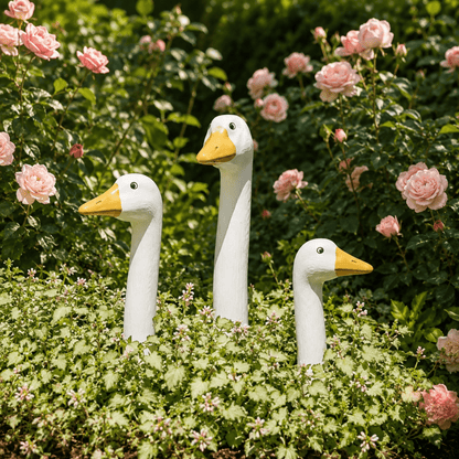 Three white peeking goose garden stakes in different sizes among pink flowers and green foliage.