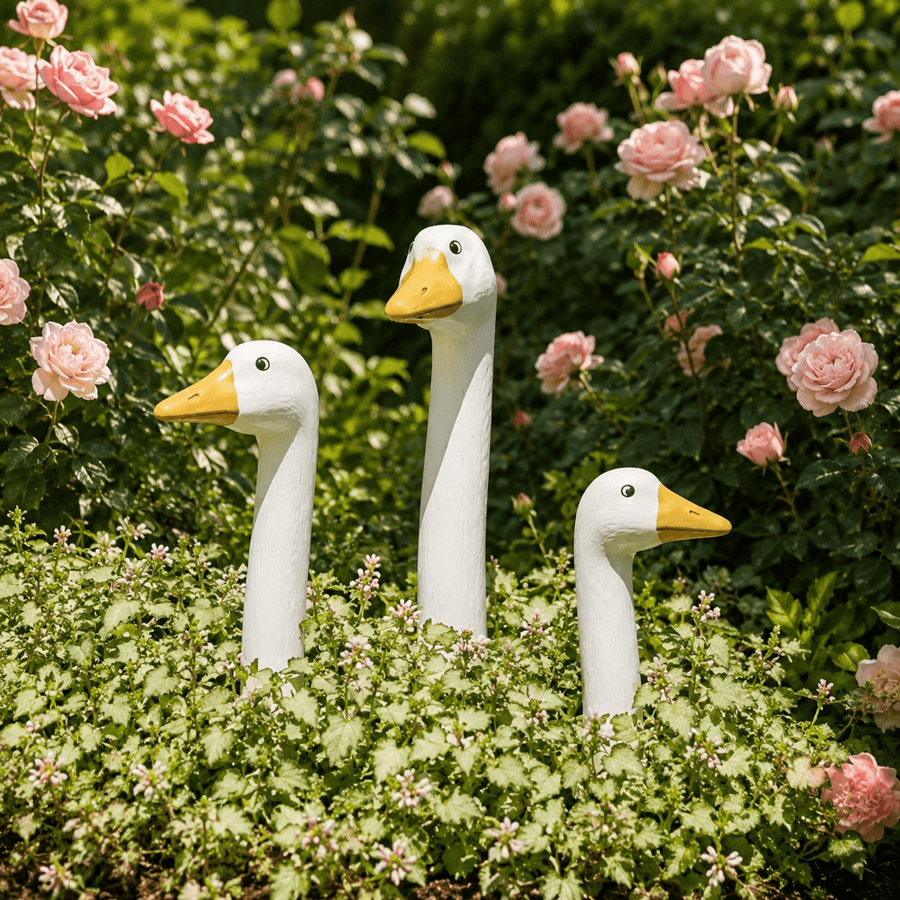 Three white peeking goose garden stakes in different sizes among pink flowers and green foliage.